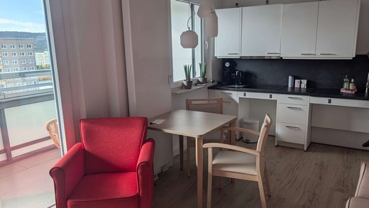 Blick in eine barrierefreie Wohnung mit Balkon, roter Sessel und offene Küchenzeile