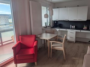 Blick in eine barrierefreie Wohnung mit Balkon, offene Küchenzeile, roter Sessel. Klick öffnet eine vergrößerte Ansicht.