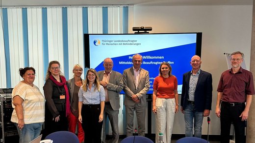 Gruppenbild der drei Beauftragten aus Sachsen, Sachsen-Anhalt und Thüringen mit Mitarbeiterinnen und zwei Mitgliedern aus den Gremien. Im Hintergrund ist ein Präsentationsbildschirm zu sehen.